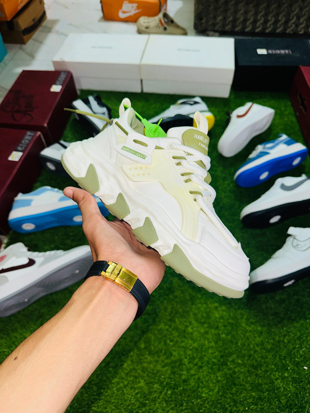 Hand holding a white sneaker with other sneakers and boxes in the background